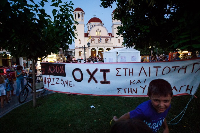 Boy by NO/OXI Syriza banner for EU referendum during Greek Eurozone crisis by Rethymno church Greece